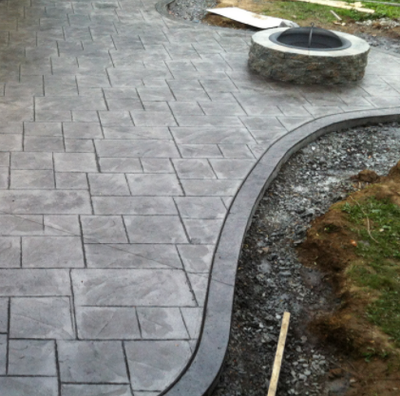 Stamped concrete colored gray and edged around front yard landscaping.